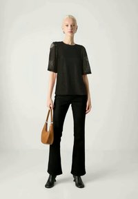 Czarny koronkowy top z krótkimi rękawami, zestawiony z szerokimi czarnymi spodniami i botkami za kostkę; trzyma brązową torebkę. Prosty, nowoczesny design.