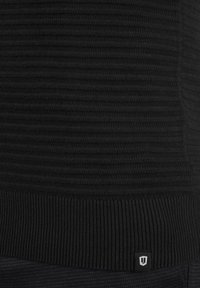 Schwarzer Strickpullover mit geripptem Muster, horizontalen Streifen und einem kleinen Logo-Tag am Saum. Weiches Material und enganliegende Passform.