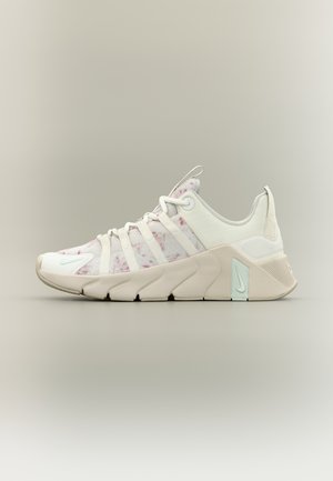 Witte en beige sportschoen met lichtroze spikkels, gesegmenteerde zool, bovenwerk van mesh en Nike-logo bij hiel en teen.