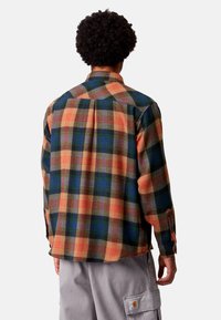 Camicia di flanella a quadri nei colori arancione, verde e blu, con colletto abbottonato, maniche lunghe e orlo spaccato. Tessuto morbido con una vestibilità comoda.