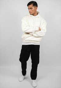 White oversized hoodie with a front kangaroo pocket, paired with black cargo pants and white sneakers. Simple design, casual fit, no patterns.