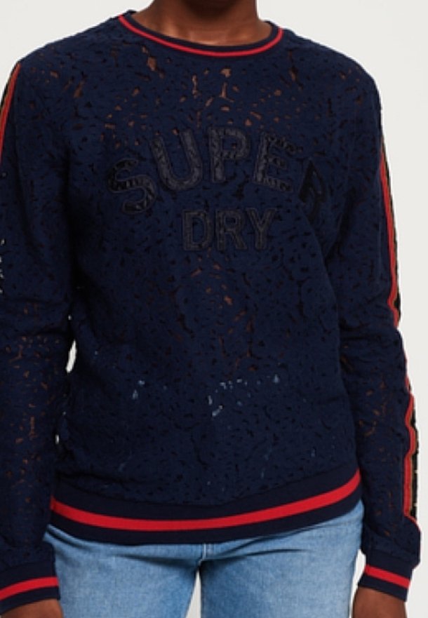 Mörkblå stickad sweatshirt med ett texturerat mönster, med "SUPER DRY" i präglade bokstäver och röda accentränder på ärmarna och nederkanten.