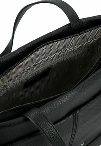 Borsa tote in pelle nera con superficie texturizzata, aperta per rivelare un interno grigio a motivo con una singola tasca con zip.