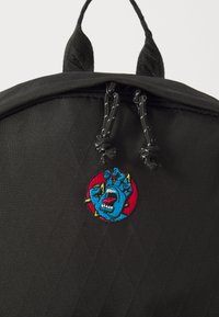 Zwarte stoffen rugzak heeft een opvallende cirkelvormige geborduurde patch met een blauw monsterontwerp en een rode achtergrond, met mooie textuurdetails.