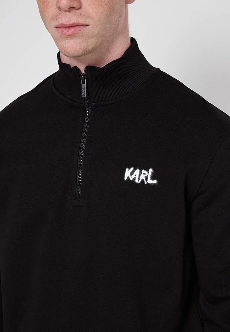 Czarna bluza z zamkiem błyskawicznym i wysokim kołnierzem, z białym haftowanym logo "KARL" na lewej piersi. Wykonana z miękkiej, teksturowanej tkaniny.