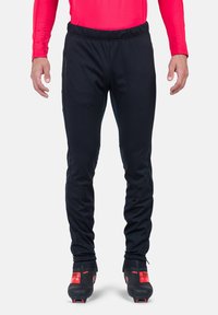 Schwarze Sporthose mit schmalem Schnitt, elastischem Bund, seitlichen Reißverschlusstaschen und kontrastierenden Reißverschlussdetails an den Knöcheln.