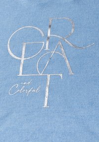 Tejido azul claro con texto metálico plateado que dice "GRANDE y Colorido" en una fuente moderna. Textura suave con variaciones sutiles.