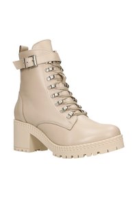 Stivaletti in pelle beige con tacco a blocco spesso, cinturino decorativo con fibbia e occhielli in metallo. Presentano una suola testurizzata e dettagli con lacci.