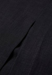 Gros plan d'un tissu noir avec un tissage texturé subtil et une couture pliée créant de douces ombres.
