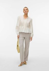 Vit texturerad blus med peplumskjort, kombinerad med ljusgrå raka byxor. Modellen håller en gul väska och bär mönstrade klackar.