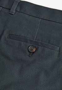 Pantaloni grigio scuro con tessuto testurizzato, chiusura a bottone sulla tasca posteriore e cuciture su misura lungo la vita.