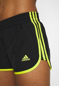 Pantalones cortos deportivos negros con acentos amarillos, que cuentan con una cintura elástica y tres rayas verticales, diseñados para brindar comodidad y movilidad.