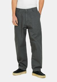 Grey cargo pants made from cotton, feature a relaxed fit, dual front pockets, and visible stitching. Paired with black shoes and a white top.