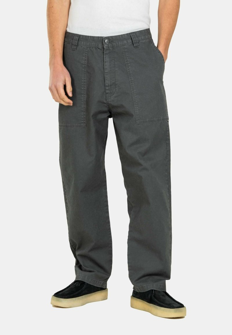 Grey cargo pants made from cotton, feature a relaxed fit, dual front pockets, and visible stitching. Paired with black shoes and a white top.