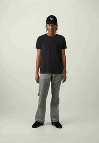 Melnas kokvilnas T-krekls, pelēkas džinsu bikses ar ķēdes detaļu, melna cepure ar logo un melnas kurpes. Vienkāršs dizains un pieguļoša silueta.