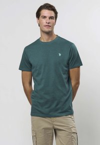 Tirkizna pamučna majica kratkih rukava s okruglim izrezom, s malim svijetlim logotipom na lijevoj strani prsa. Prikladna za ležerni stil.