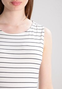 Top bez ramiączek z okrągłym dekoltem, z cienkimi granatowymi paskami na jasnobeżowym tle. Wykonany z gładkiego, rozciągliwego materiału.