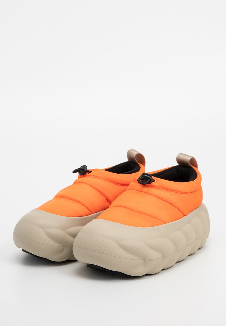 Helle orange gepolsterte Slipper mit beigen, dicken, strukturierten Sohlen und schwarzen verstellbaren Schnüren oben.