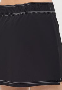 Falda de baño negra con cinturilla elástica, que presenta costuras blancas a lo largo del dobladillo y la cintura para un diseño simple y funcional.
