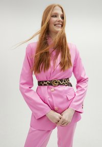 Rosa blazer och matchande byxor med en strukturerad passform. Bältet har leopardmönster och en gyllene cirkulär spänne. Slät textur, skräddarsydd design.