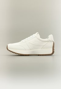 Λευκό αθλητικό παπούτσι με λείο συνθετικό επάνω μέρος, κλείσιμο με κορδόνια και καφέ λαστιχένια σόλα με ανάγλυφο ζιγκζαγκ μοτίβο.