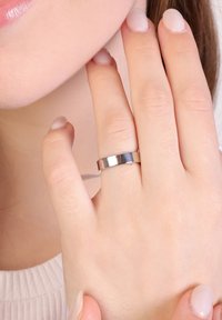 Zilveren metalen ring met een vlak, gepolijst oppervlak, gedragen aan een hand met natuurlijke, lichtgekleurde nagels. De huidskleur lijkt licht.