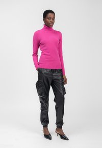Fuchsia-Turtleneck-Pullover kombiniert mit schwarzen Leder-Cargo-Hosen mit Seitentaschen und schwarzen spitzen Absatzschuhen.