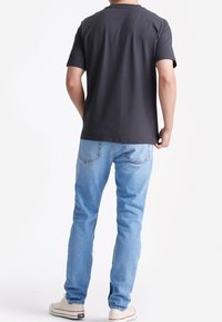 Zwart T-shirt met korte mouwen en een ronde hals, gecombineerd met lichtblauwe spijkerbroek en witte sneakers, gezien vanuit de achterkant.