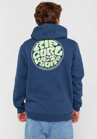 Felpa blu navy con una grande grafica circolare di colore verde chiaro sul retro, che presenta un testo stilizzato. Tessuto misto cotone con polsini a coste.