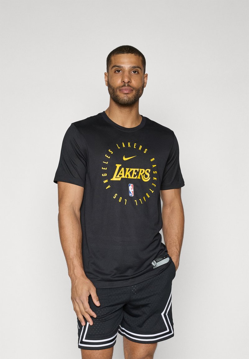 T-shirt noir Nike avec le logo circulaire jaune "Lakers", à manches courtes et col rond ; associé à un short en mesh noir avec des accents blancs.