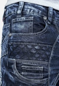 Jeans in denim scuro con un design aderente, dotati di più tasche, accessori in metallo argentato e un motivo trapuntato testurizzato lungo il lato.