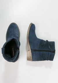 Granatowe zamszowe botki za kostkę z dekoracyjnymi wycięciami, bocznym zamkiem błyskawicznym i niskim, teksturowanym beżowym obcasem. Płaskie w środku z wzmocnionymi szwami.