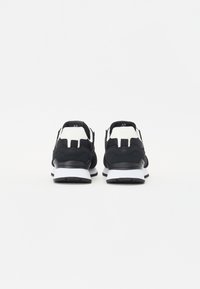 Baskets en suède noir avec des accents blancs ; dotées d'une semelle rembourrée et d'un motif texturé à l'arrière. Numéro de modèle visible au niveau du talon.