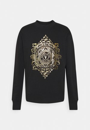 Zwarte lange mouwen sweatshirt met een centraal sierlijk gouden embleem met de tekst "Versace Jeans Couture" en decoratieve bloemmotieven.