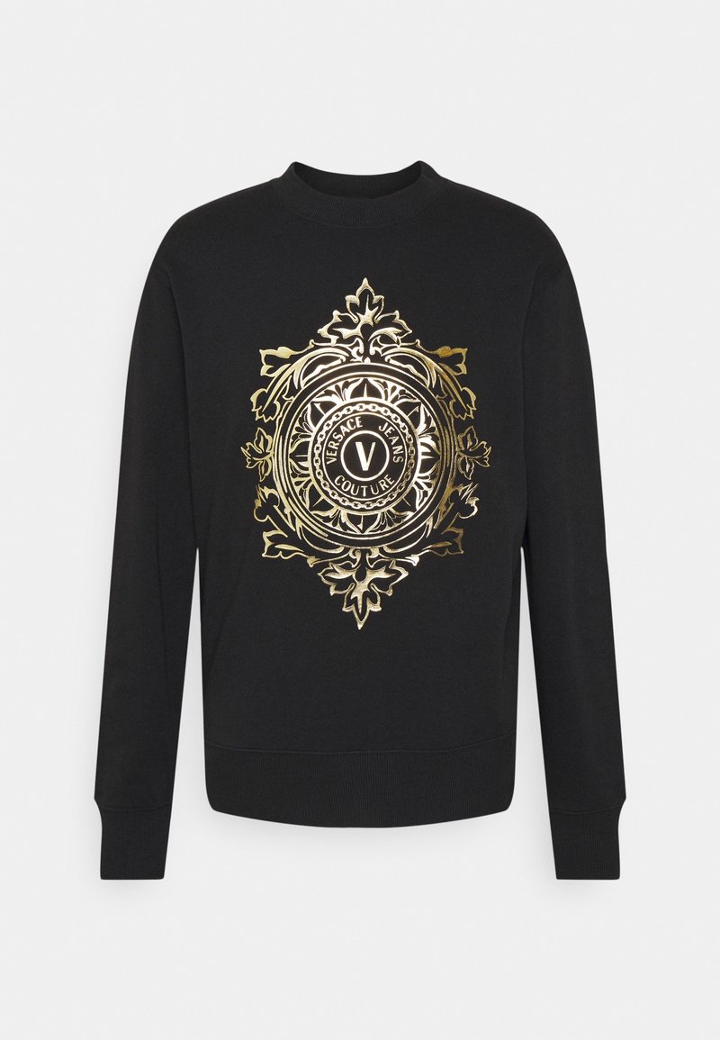 Sweat-shirt noir à manches longues avec un emblème doré orné au centre affichant le texte « Versace Jeans Couture » et des motifs floraux décoratifs.