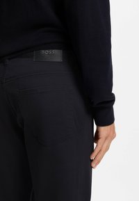 Granatowe bawełniane spodnie z etykietą "BOSS" z skóry na pasku, z usztywnionymi kieszeniami i subtelnymi detalami przeszyć.