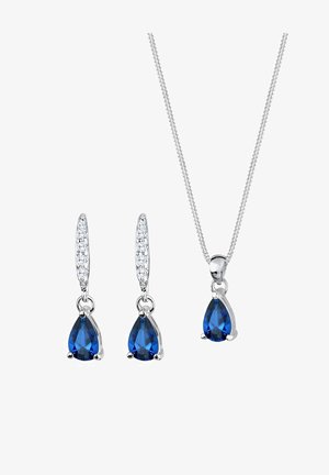 Conjunto de joyería en tono plateado con piedras azules en forma de pera y acentos claros, que incluye pendientes colgantes a juego y un collar con cadena.