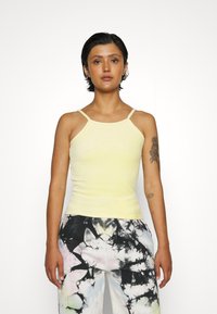 Kollane, kehakujuline tank top õhukeste rihmadega ja ümmarguse kaelusega, millel on hõredalt tekstureeritud pind ja tikand detail rindkere piirkonnas.