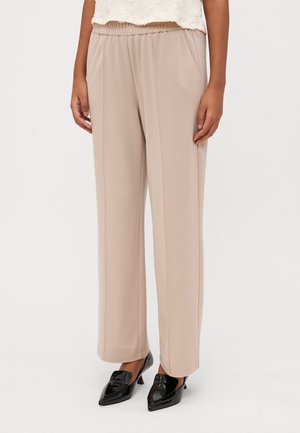 Beige wijde broek met een elastische tailleband en zijzakken, gemaakt van gladde stof. In combinatie met puntige zwarte gepatineerde leren hakken.