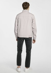 Jasnoszara kurtka wykonana z miękkiego, lekkiego materiału, z wysokim kołnierzem i ściągaczami, w połączeniu z ciemnymi dżinsami i białymi trampkami.