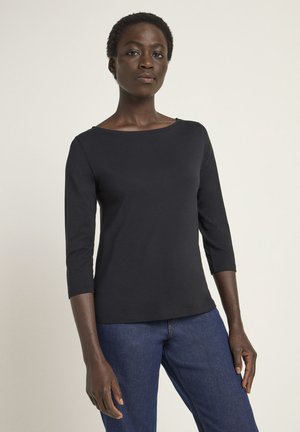 Schwarzes, tailliertes Langarmshirt mit rundem Halsausschnitt und mittellangen Ärmeln, kombiniert mit dunkelblauen Jeans. Glatte Textur, einfaches Design.