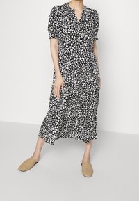 Schwarz-weißes Leopardenmuster-Midikleid mit kurzen Puffärmeln, einem V-Ausschnitt und einem fließenden Saum. Kombiniert mit hellbraunen, gewebten Slippern.