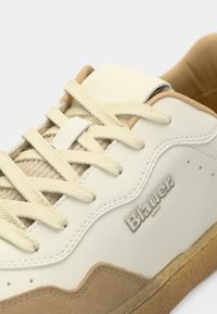 White sneaker with tan suede accents and textured rubber sole. Features round laces, logo on the side, and a padded collar for comfort.