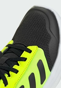 Black and neon yellow athletic shoe with mesh upper, padded collar, black laces, and white sole. Features textured accents and side stripes.