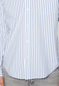 Lichtblauwe en witte gestreepte button-up shirt met een zak, lange mouwen en een afgeronde zoom. Gemaakt van gladde katoenstof.