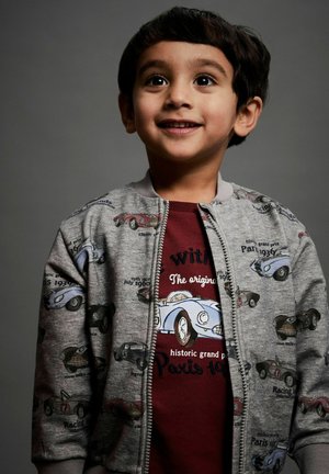 Gray bomber jacket with car prints over a maroon t-shirt featuring graphic text. The bomber has a zipper and ribbed cuffs.