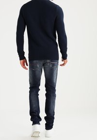 Marinblå ribbstickad tröja med långa ärmar, tillsammans med slim fit, blekblå jeans med bakfickor och diskret slitningar. Vita sneakers.