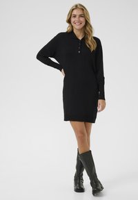 Black knitted dress with long sleeves and a polo collar, featuring a buttoned placket and ribbed hem, paired with knee-high black boots.