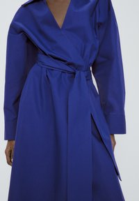 Lång blå omlottklänning i en bomullsblandning, med djup V-ringning, långa Ärmar och knytning i midjan samt asymmetrisk fåll.