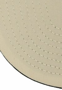 Beige fabric cap with a textured surface, circular shape, and contrasting black edging. Visible stitching lines create a pattern.